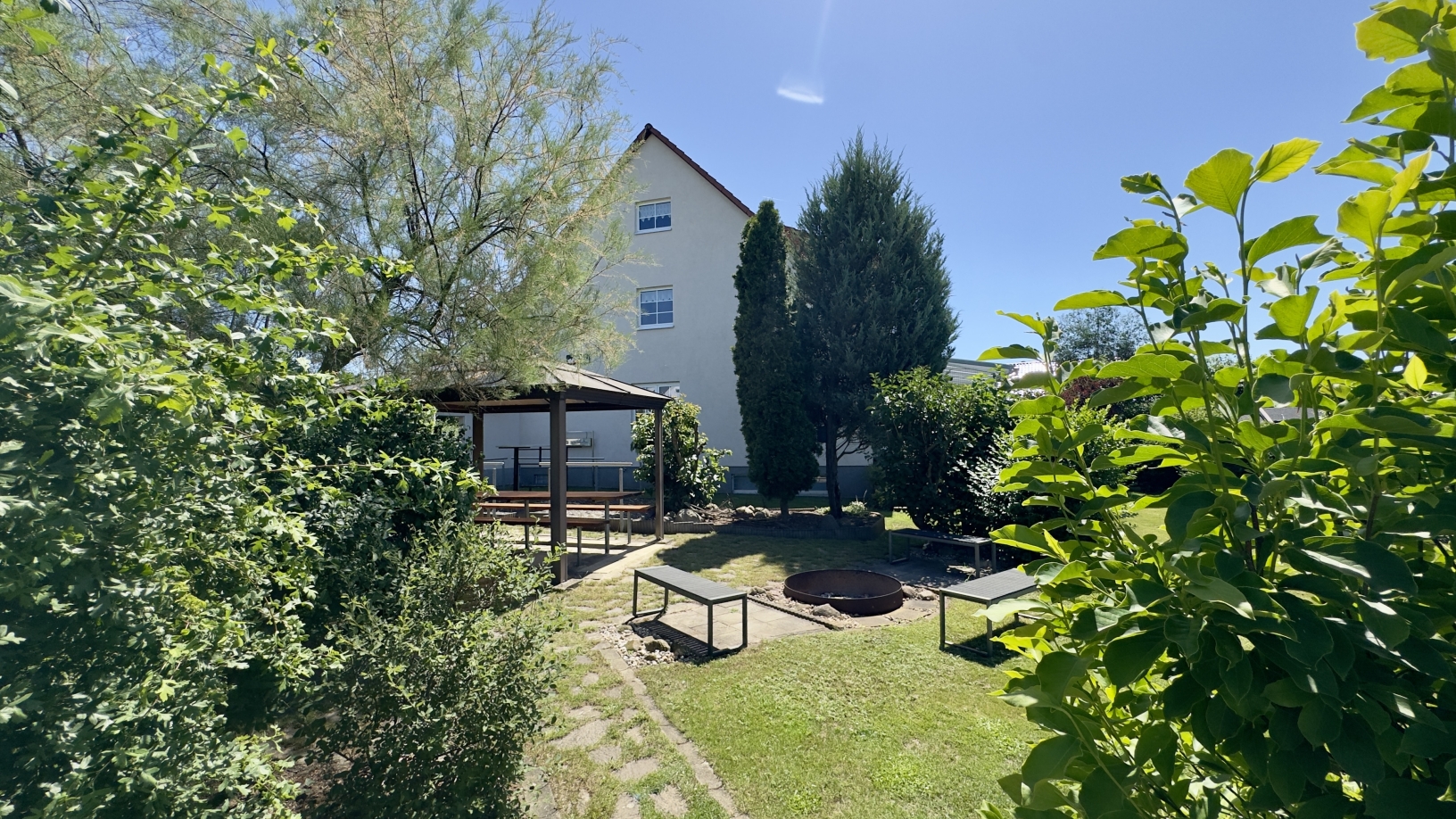 Blück über die Feuerstelle und den Pavillon auf das Haus
